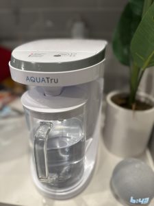 AquaTru countertop water purifier filtering tap water into a glass carafe on a modern kitchen counter, showcasing a compact reverse osmosis water filtration system for clean, great-tasting drinking water.