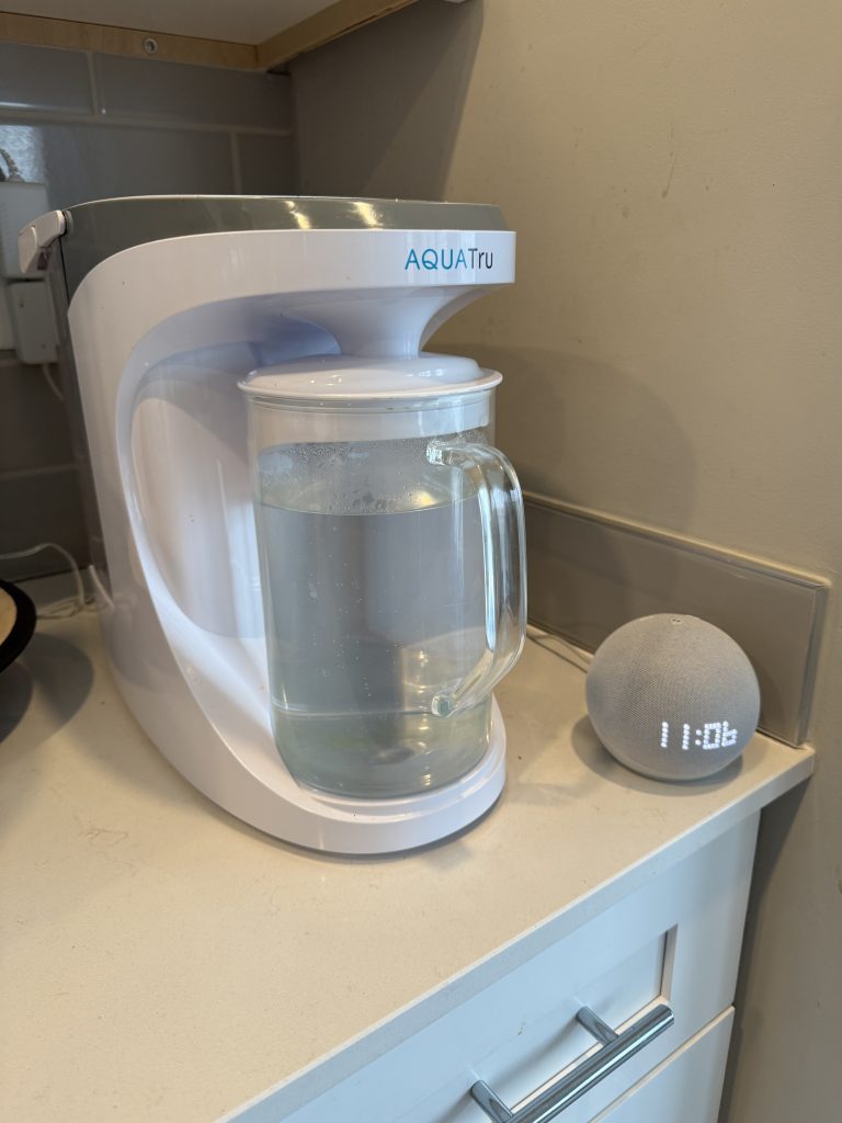 AquaTru Carafe sitting on kitchen counter with glass carafe full of filtered water
