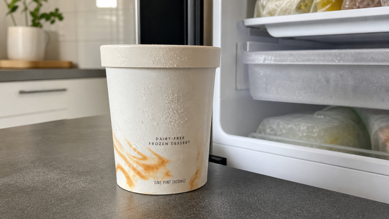 Pint of dairy-free frozen dessert on a kitchen counter next to an open freezer, representing the So Delicious Salted Caramel Cluster recall