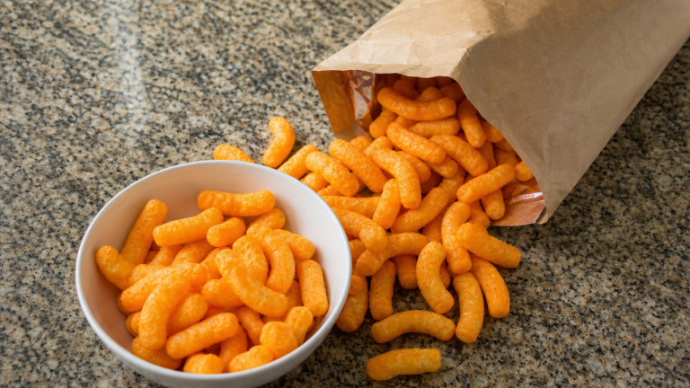 Bag of orange cheese puff snacks spilled into a bowl on a kitchen counter, representing the Frankie's Organic vegan cheddar puffs recall