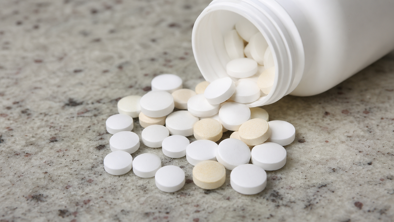 Close-up of white and slightly discolored round tablets spilled from a pill bottle onto a counter