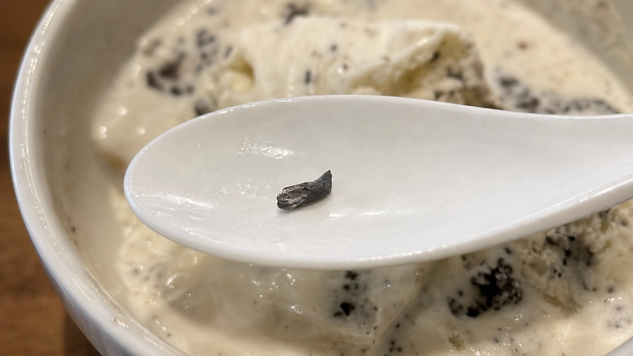 Close-up of a small metal fragment resting on a spoon over melted ice cream