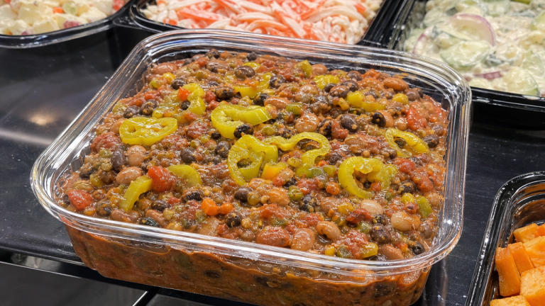 Clear deli tray of salsa bean dip with peperoncini peppers on top